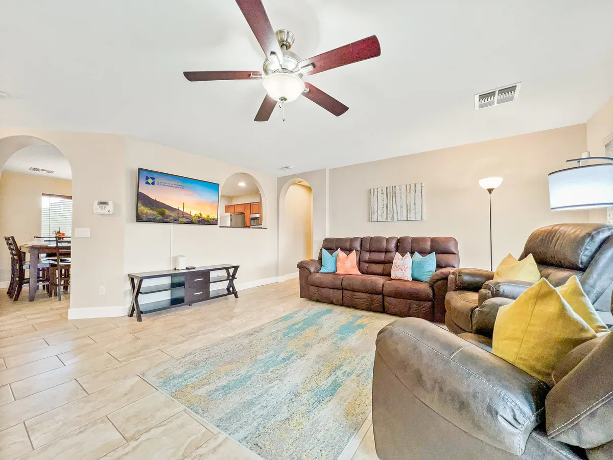 A cozy living room with a comfortable sofa, decorative pillows, a TV displaying scenic artwork, stylish lighting, and inviting ambiance. The space is arranged for both group gatherings and intimate conversations, with soft natural light enhancing the atmosphere.