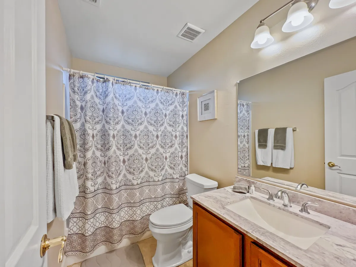 A bright and calming guest bath with a bathtub and shower curtain, a double vanity with a wide sink, and a large mirror. The space supports both quick morning routines and leisurely evening soaks, making it suitable for group and family use.
