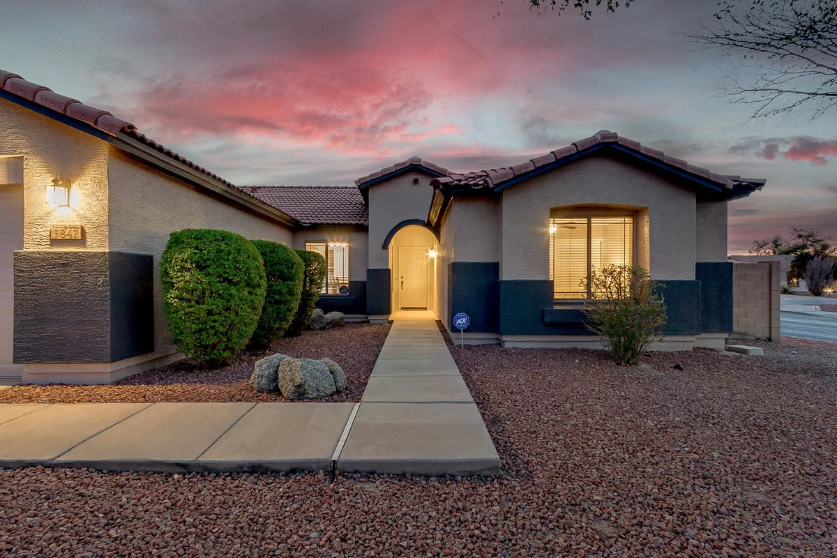 A charming view of the home's front door framed by neatly landscaped bushes and a wide pathway, set against a beautiful sky. This entrance scene signals a warm welcome and easy access to Queen Creek's family attractions.