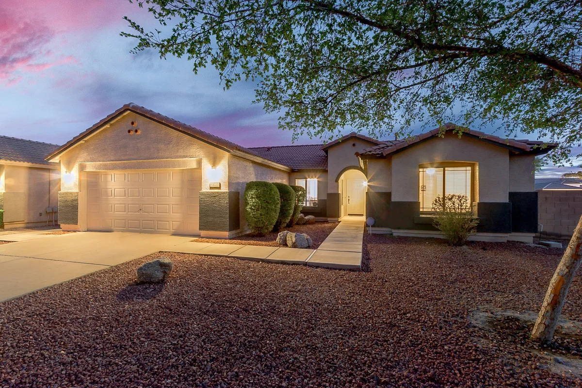An exterior shot of the front porch and garage door, framed by landscaped pathways, bushes, and trees. The garage is clearly visible, hinting at its accessibility and security for guests.