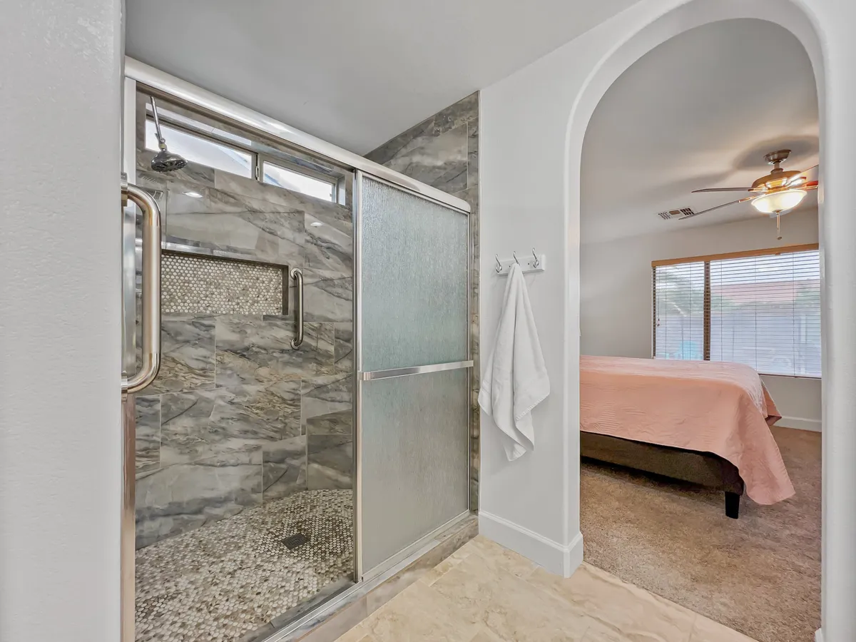 A tranquil bathroom featuring a glass shower enclosure with textured wall tiles, and a unique architectural archway that hints at a connected bedroom. The space feels modern and peaceful, perfect for relaxing showers and unwinding before bedtime.