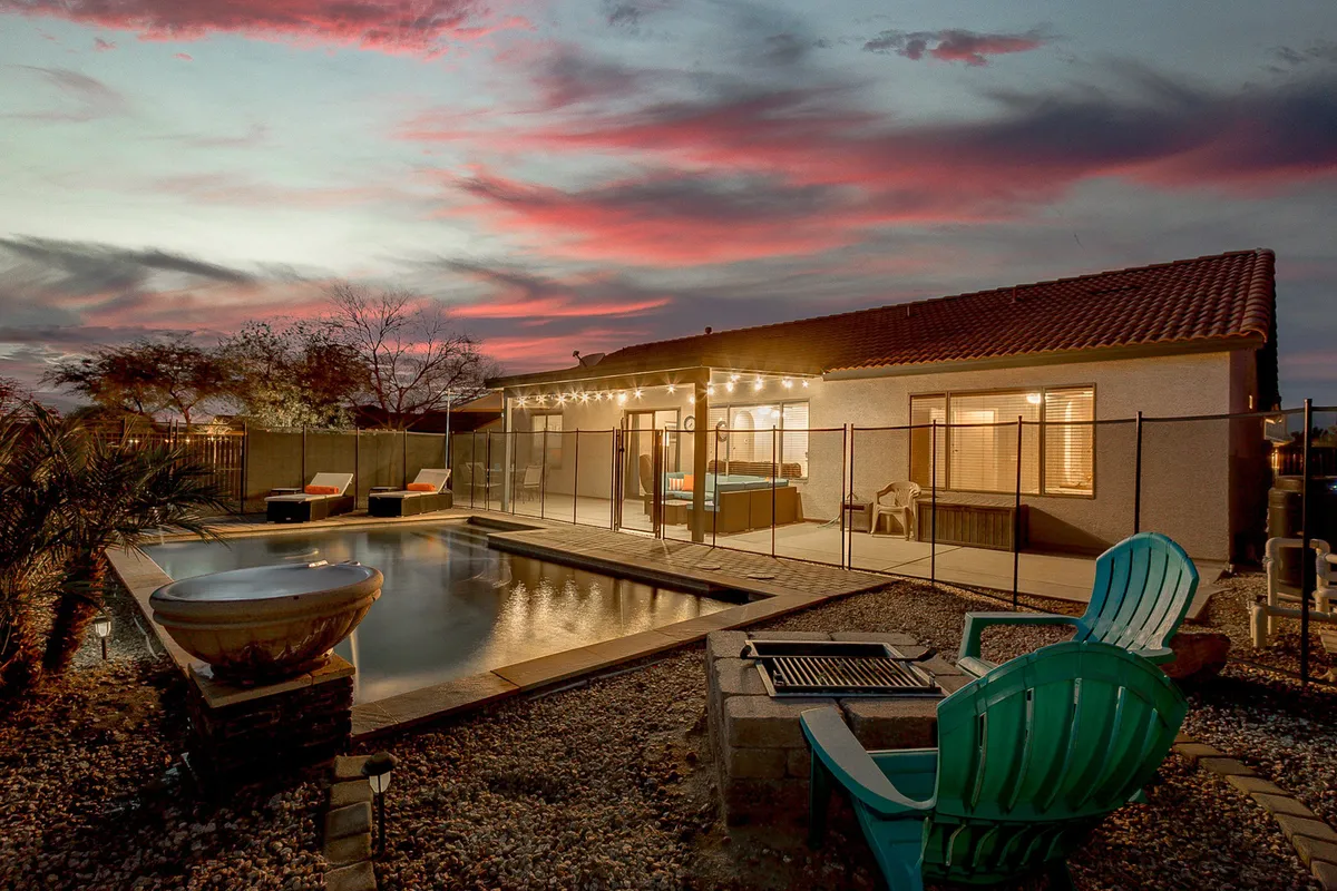 A beautiful exterior scene at dusk features a sparkling swimming pool, an inviting outdoor seating area, and a dining space illuminated by string lights. The sky is painted in soft sunset hues, creating an atmosphere perfect for evening gatherings and celebrations.