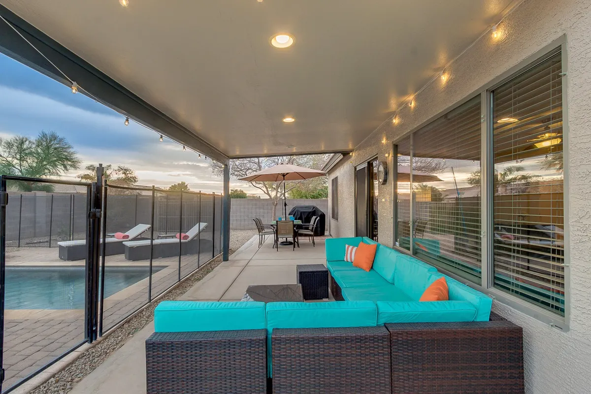 This exterior view spotlights a turquoise sectional sofa and a dining table with umbrella beside a sparkling swimming pool. The area is designed for outdoor dining, lounging, and social gatherings—echoing the spirit of Arizona's outdoor lifestyle.