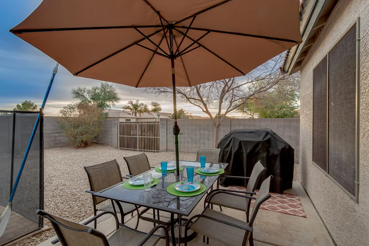 A cheerful backyard setup with a dining table under a large umbrella and a grill nearby, set for outdoor meals and barbecues. The space is designed for relaxing, dining, and celebrating with friends and family in a comfortable, shaded setting.