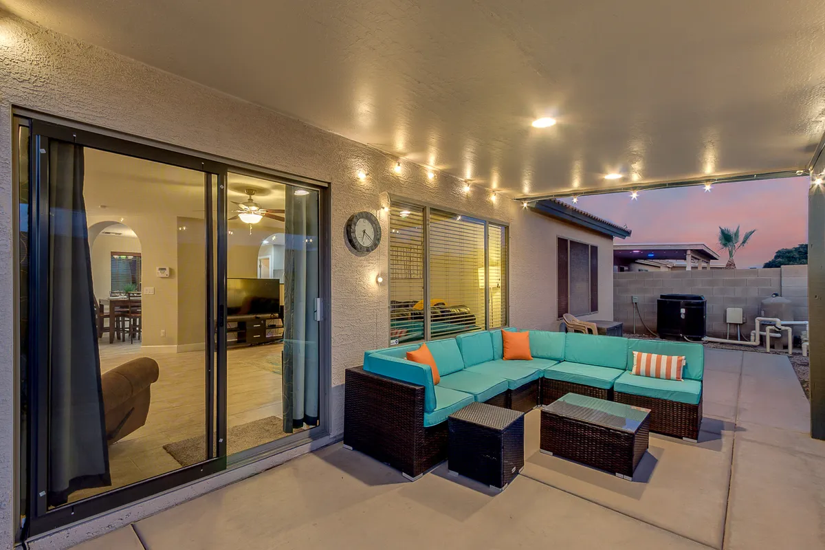 A relaxed, social exterior setting with turquoise outdoor seating, glowing string lights, and a decorative clock on the wall. The scene is ideal for casual evening get-togethers, family barbecues, or quiet moments with a book.